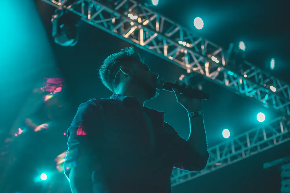 A singer in profile at the microphone, in teal light