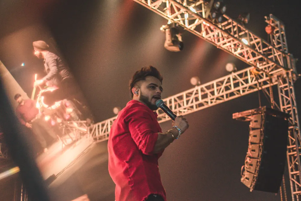 A singer in a red shirt, the truss and speakers behind him