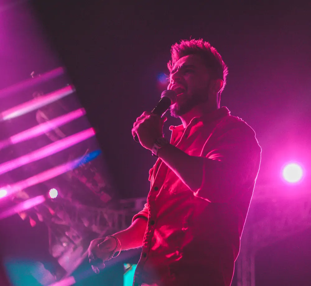 A singer in a red shirt, mid-note, under magenta light