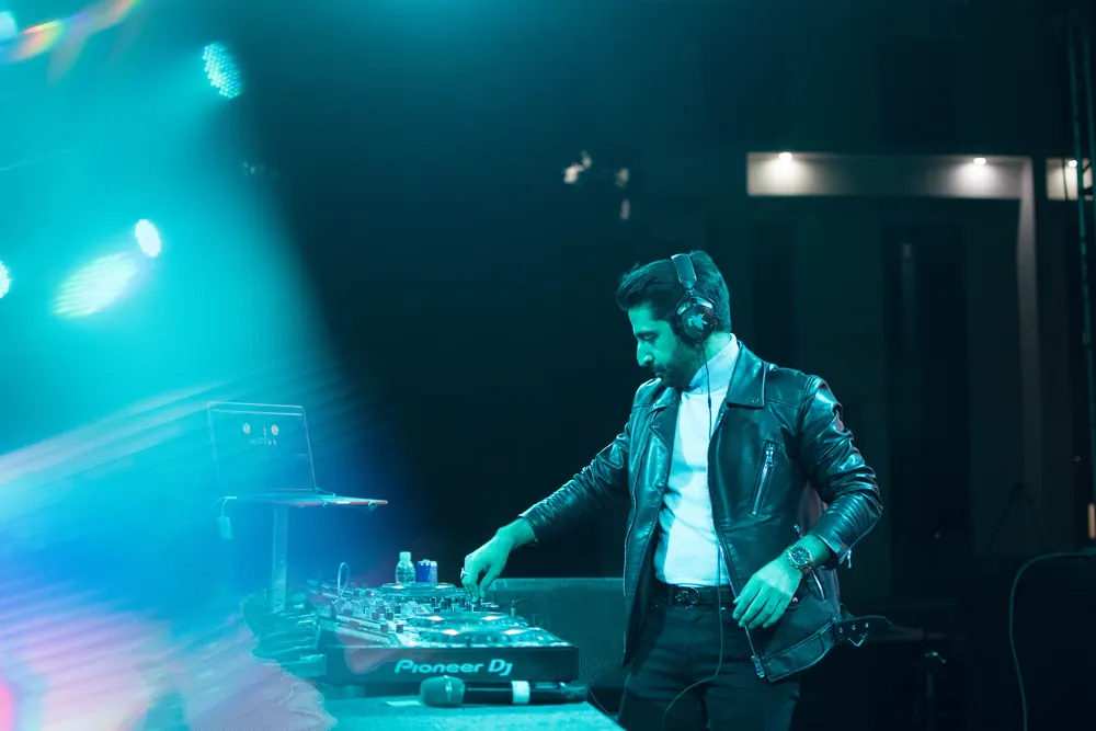 A DJ at the decks, a beam of teal light across the stage