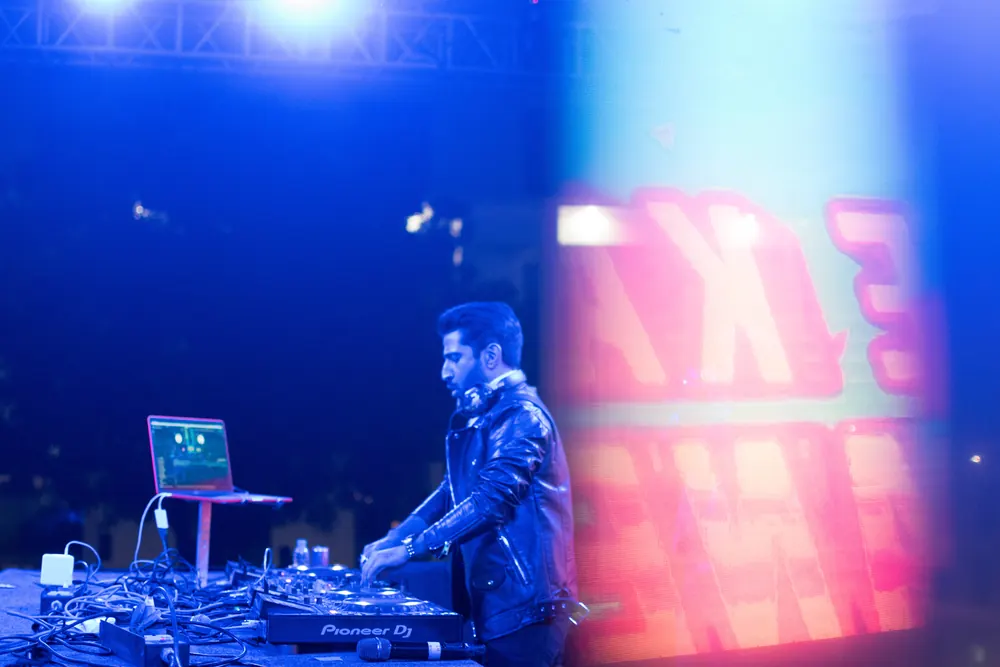 A DJ at the decks beside a laptop, in blue light