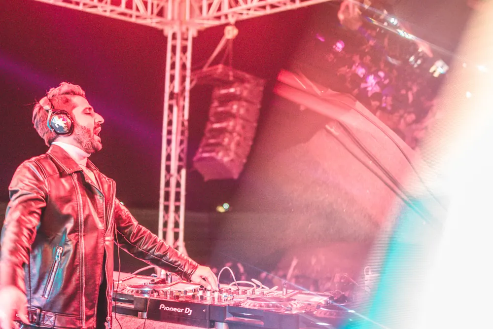 A DJ in headphones, shouting, under the truss in pink light