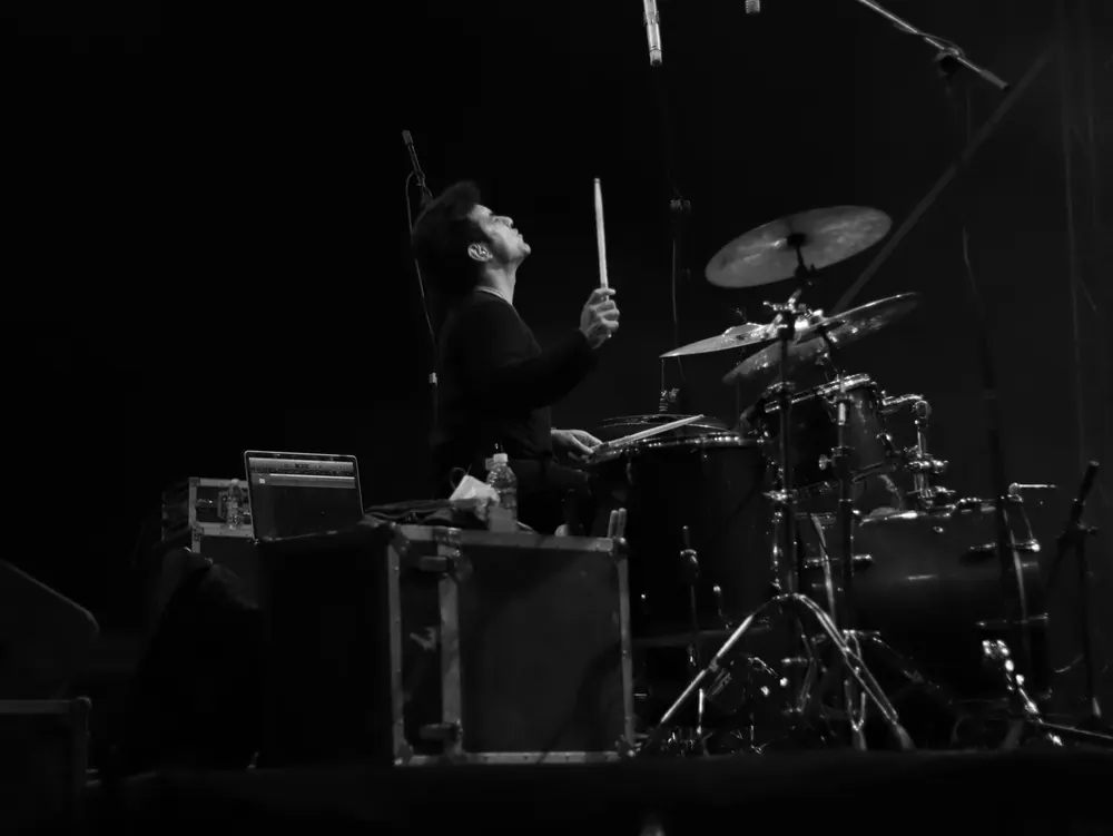 A drummer, sticks raised, in black and white