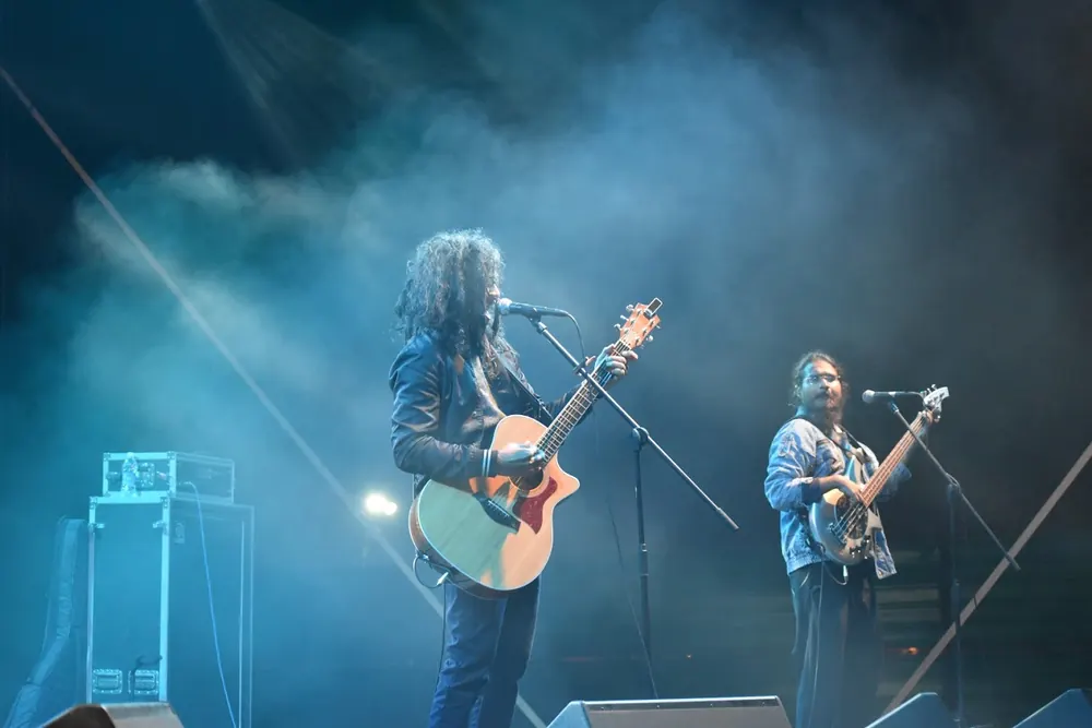 Two guitarists on a smoky stage in blue light
